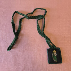 Brown embroidered fabric braided scapular. The front features a half-length image of Saint Jude, and the back features Our Lady of Guadalupe. Scapular badge measures 1.35 inches wide, 1.45 inches high. Scapular wire length: panel to panel: 14.5 inches. Escapulario de tela color café bordado  En la parte delantera muestra imagen de San Judas,  en la parte de atrás la Virgen de Guadalupe. Medidas de la insignia escapular 1.35 pulgadas ancho  de la insignia escapular, 1.45 pulgadas alto Longitud del cable escapular: panel a panel 14.5 pulgadas.