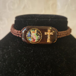Pulsera de Hilo en color café, tamaño ajustable con un centro de Imagen de el Ángel de la Guarda,  impresa a colores  y la imagen de una cruz al lado. Centro de la Pulsera de madera con imagen mide 1 Pulgada de ancho ½ Pulgada de alto . Brown thread bracelet, adjustable in size, with a center image of Guardian Angel, printed in color and a cross on the side. The wooden bracelet center with the image measures 1 inch wide and 1/2 inch tall.