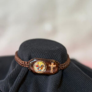 Pulsera de Hilo en color café, tamaño ajustable con un centro de Imagen de la Divina Providencia,  impresa a colores  y la imagen de una cruz al lado. Centro de la Pulsera de madera con imagen mide 1 Pulgada de ancho ½ Pulgada de alto . Brown thread bracelet, adjustable in size, with a center image of Divine Providence, printed in color and a cross on the side. The wooden bracelet center with the image measures 1 inch wide and 1/2 inch tall.