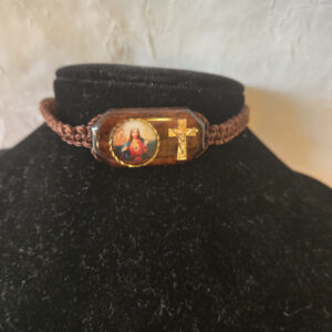 Pulsera de Hilo en color café, tamaño ajustable con un centro de Imagen de medio cuerpo del Sagrado Corazón  impresa a colores  y la imagen de una cruz al lado. Centro de la Pulsera de madera con imagen mide 1 Pulgada de ancho ½ Pulgada de alto .5 Oz Brown thread bracelet, adjustable in size, with a center half-length image of the Sacred Heart printed in color and a cross on the side. The wooden bracelet center with the image measures 1 inch wide and 1/2 inch tall.